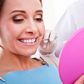 Woman in dental chair looking at smile in mirror